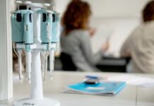 Przegląd informacji z rynku medycyny i biotech na pierwszym planie pipety laboratoryjne, biurko z papierami, w tle osoba trzymająca dokumenty