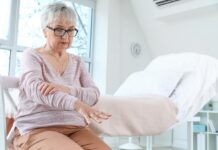 Choroba Parkinsona: pacjenci i neurolodzy czekają na program opieki koordynowanej starsza kobieta siedzi na łóżku szpitalnym, wyciąga rękę przed siebie - drżenie rąk