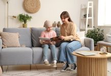 Nowotwory dziecięce – rzadkie tylko z nazwy dziecko siedzi na kanapie z książką w ręku, obok jest mama/nauczycielka, która tłumaczy