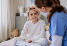 Czym różnią się nowotwory dziecięce od nowotworów u dorosłych? dziecko siedzi na łóżku lekarka sprawdza mu temperaturę