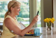 Systemy CGM pozwalają na szybką optymalizację terapii kobieta siedzi w kuchni nad talerzem z jedzeniem. sprawdza w telefonie poziom glikemii