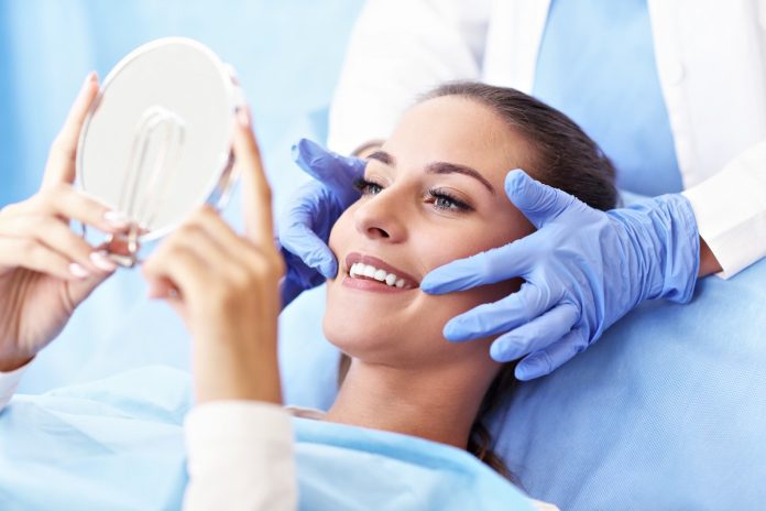 usmiech Oral Care pacjentka na fotelu dentystycznym, trzyma lusterko w rękach i sprawdza swój uśmiech