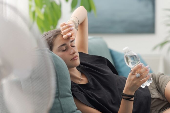 Exhausted,Young,Woman,At,Home,During,The,Summer,Heatwave,,She młoda kobieta leży na kanapie wyczerpana w ręce ma butelkę wody