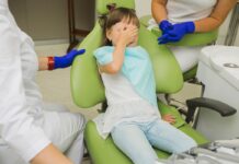 Ortotropia jest niezgodna z wiedzą medyczną mała dziewczynka siedzi na fotelu dentystycznym i zakrywa oczy ze strachu