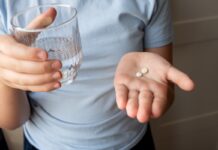 Antybiotykoodporność jest jednym z najpoważniejszych zagrożeń zdrowotnych XXI wieku Pill and glass with water in the hand of child. Healthcare from pharmacy. Kid sit at home because of illness.
